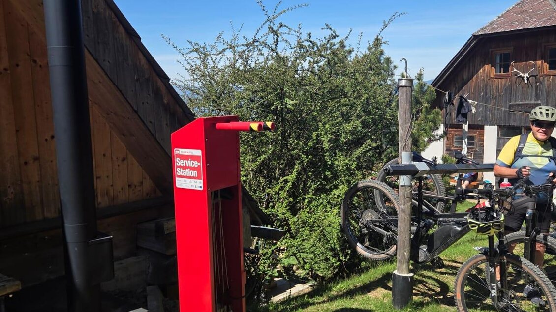 Eine rote Werkstattecke für Fahrräder steht neben einem Gebäude. Im Hintergrund sind Bäume und andere Fahrräder zu sehen. | © Roman Gruber