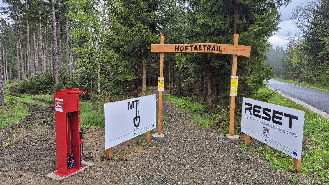 Eingang zum Hoftaltrail in einem Waldgebiet. Links steht eine rote Station, und es gibt Schilder mit weiteren Informationen. | © Christian Webersink