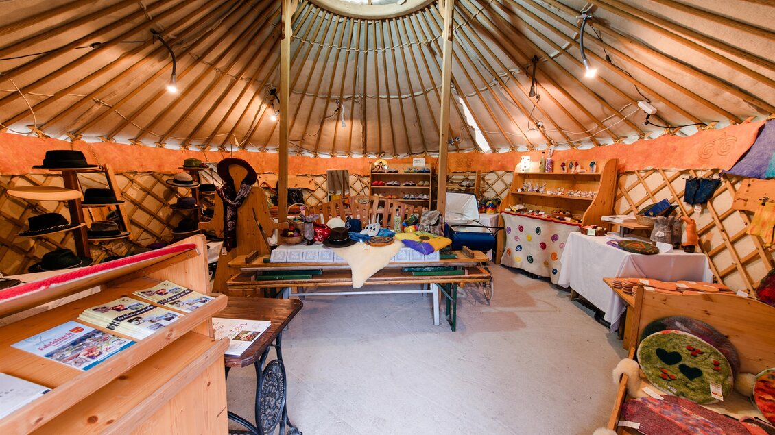 <p>Ein gemütlicher Raum in einem traditionellen Jurten-Design. Die Wände sind mit Holz und bunten Gegenständen dekoriert, und es gibt verschiedene Tische und Regale mit Handwerk.Wollgenuss Naturprodukte in Edelsbach bei Feldbach</p> | © vulkanland.at florphotography