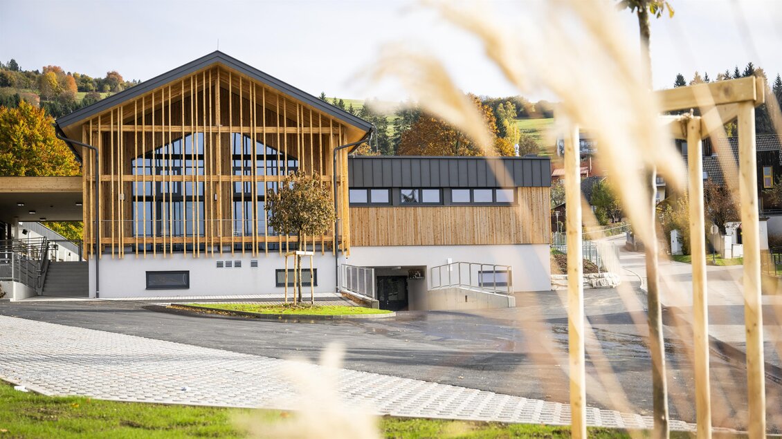 Ein modernes Gebäude mit Holzverkleidung und großen Fenstern. Umgeben von grünem Rasen und herbstlichen Bäumen. | © Gemeinde Neumarkt in der Steiermark