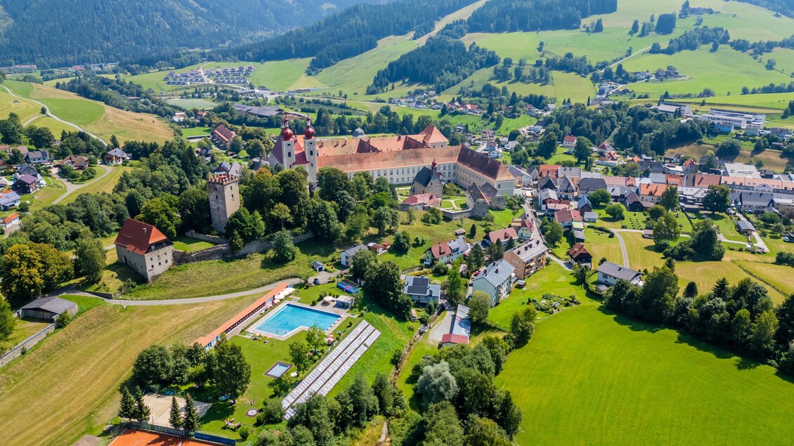 Eine malerische Landschaft mit einer kleinen Stadt und historischen Gebäuden. Grüne Wiesen sowie ein Pool und Tennisplätze sind sichtbar. | © TV Murau