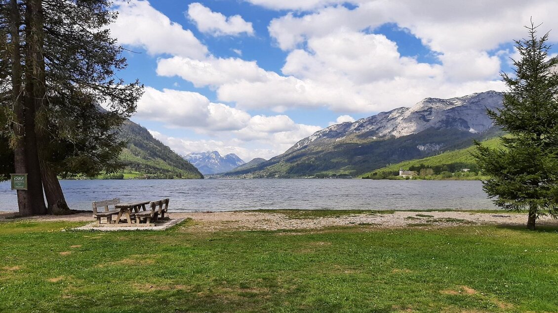 Ein malerischer See umgeben von Bergen und Bäumen. Der Himmel ist teilweise bewölkt und das Gras ist grün. | © Steinegger