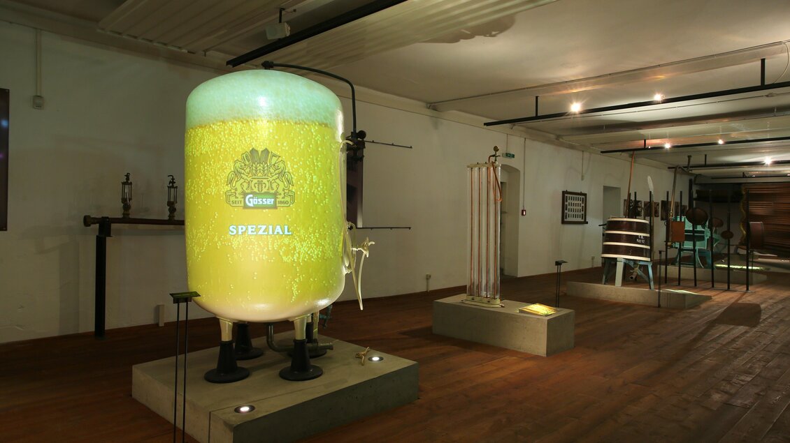 Ein Brauereimuseum mit einem großen, beleuchteten Bierbehälter. Im Hintergrund sind verschiedene Brauereigeräte zu sehen. | © Brauunion