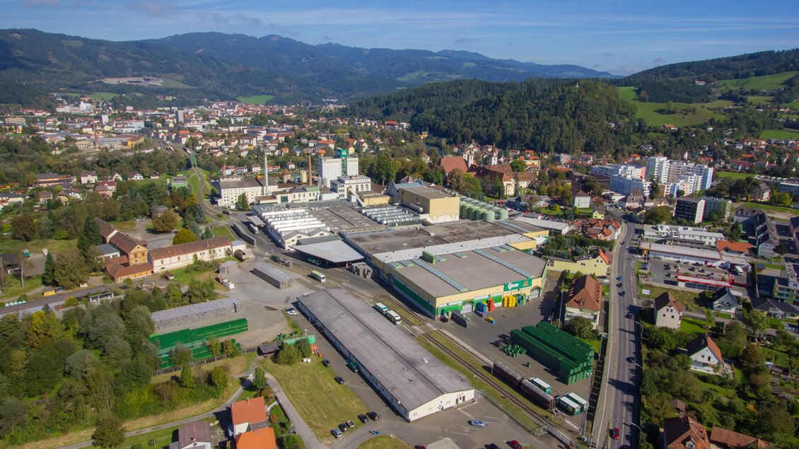 Eine Stadtansicht mit einer großen Industrieanlage und umliegenden Wohngebieten. Die Landschaft ist von Hügeln und Bäumen umgeben, mit klaren blauen Himmel. | © Brauunion