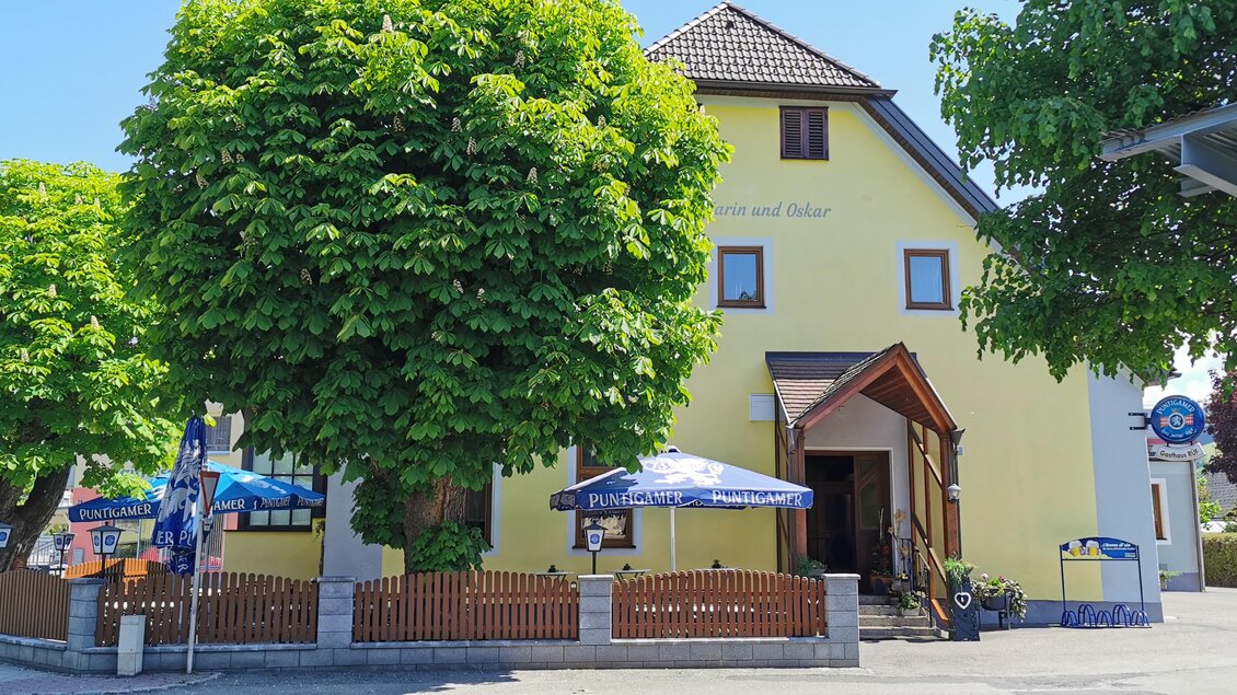 Ein gelbes Gebäude mit großen Bäumen davor. Es gibt mehrere Tische im Freien mit Sonnenschirmen. | © Gasthaus Rüf-Peterwirt