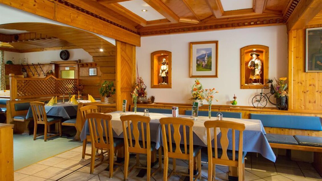 Ein gemütliches Restaurant mit Holzmobiliar und blauen Tischdecken. An den Wänden hängen dekorative Bilder und frische Blumen schmücken die Tische. | © Gasthof zum Schwarzen Adler