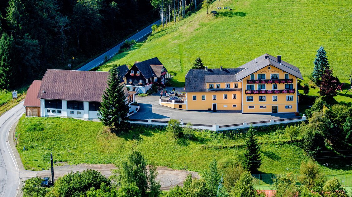 Ein malerisches Hotel auf einer grünen Wiese, umgeben von Bäumen. Die Straße führt sanft am Gebäude vorbei und bietet einen Blick auf die umliegende Natur. | © Gasthof Landhotel Hubmann