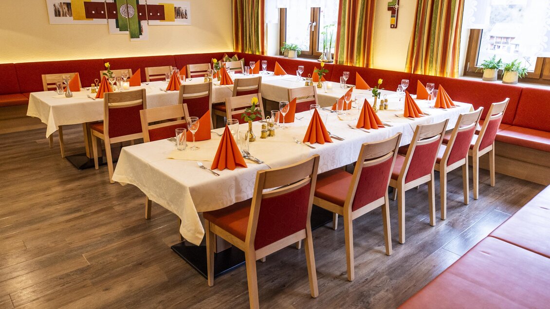 Ein schön gedeckter Tisch in einem Restaurant mit orangefarbenen Servietten. Die Umgebung ist hell und einladend mit bunten Vorhängen und Pflanzen. | © Gasthof Landhotel Hubmann