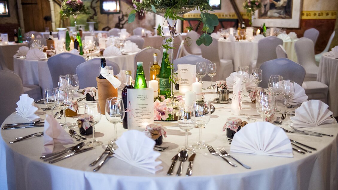 Ein elegant dekorierter Tisch für eine Feier, mit weißen Tischdecken und stilvollem Geschirr. Blumenarrangements und Kerzen sorgen für eine festliche Stimmung. | © Gasthof Landhotel Hubmann