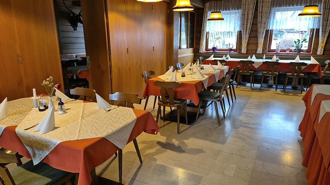 Ein gemütliches Restaurant mit Holzmöbeln und orangefarbenen Tischdecken. Die Tische sind für Gäste vorbereitet und es gibt sanfte Beleuchtung. | © TV Murau