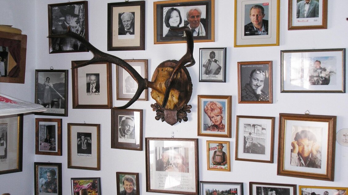 <p>Eine Wand voller gerahmter Fotos und Portraits, die verschiedene Personen zeigen im Gasthof Veit. In der Mitte hängt ein Geweih, das einen rustikalen Akzent verleiht.</p> | © Gasthaus Veit