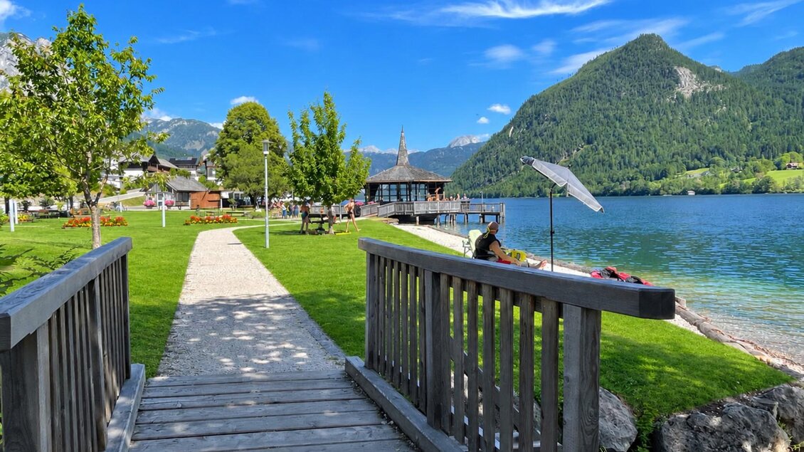 Die Brücke im Gemeindepark in Grundlsee führt direkt auf den Weg zum Musikpavillon, vorbei am Seeufer des Grundlsees und bunten Blumen. | © Tourismusverband Ausseerland