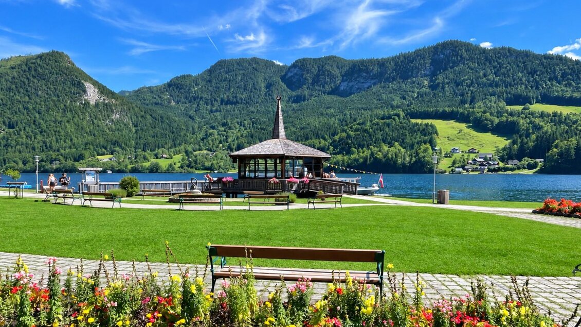 <p>Der schöne Gemeindepark am Grundlsee mit dem Muisikpavillon und blühenden Blumen. Im Hintergrund sind grüne Berge und ein blauer Himmel zu sehen.</p> | © Tourismusverband Ausseerland