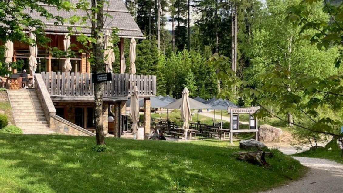 Der Genussgarten ist ein gemütlicher Imbissplatz umgeben von Bäumen. Inmitten einer grünen Wiese am See  stehen Tische unter Sonnenschirmen. | © TVB Ausseerland Salzkammergut (c) Heike Temmel