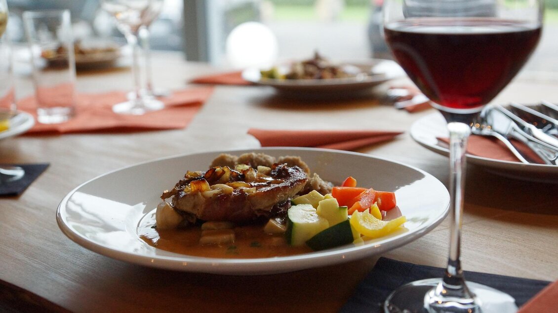 Ein lecker angerichteter Teller mit gegrilltem Fleisch und frischem Gemüse liegt auf einem Tisch. Dazu steht ein Glas Rotwein. | © Pixabay