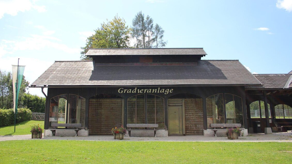 Ein Gebäude mit einem modernen Holzdesign und großen Fenstern. Es steht in einer grünen Umgebung mit Bäumen und einer gepflegten Rasenfläche. | © Viola Lechner