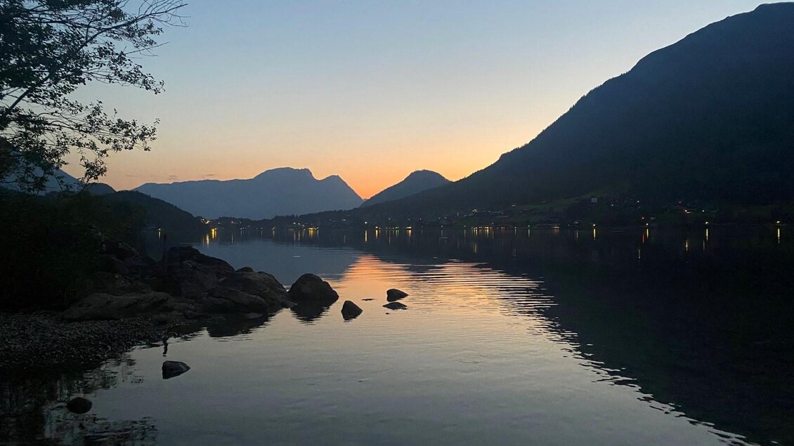 Der malerische Grundlsee bei Sonnenuntergang, umgeben von den Bergen des Ausseerland Salzkammergutes. Das Wasser spiegelt die sanften abendlichen Farben des Himmels wider. | © Bettina Scheck