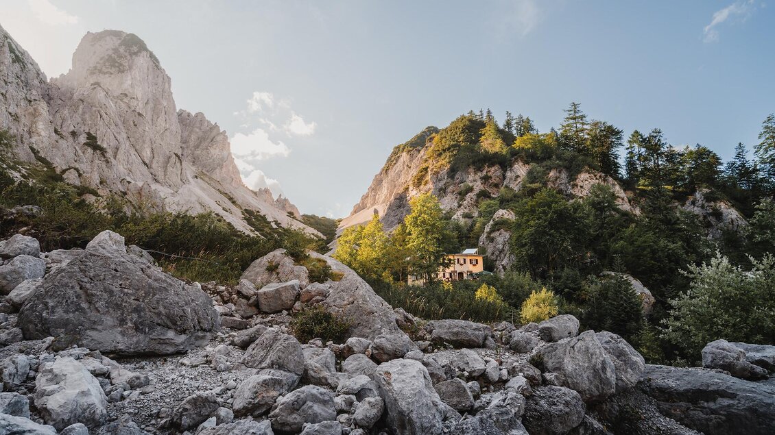 Eine malerische Berglandschaft mit hohen Felsen und grünen Bäumen. Im Hintergrund ist ein kleines Haus zu sehen, umgeben von Natur. | © TV Gesäuse