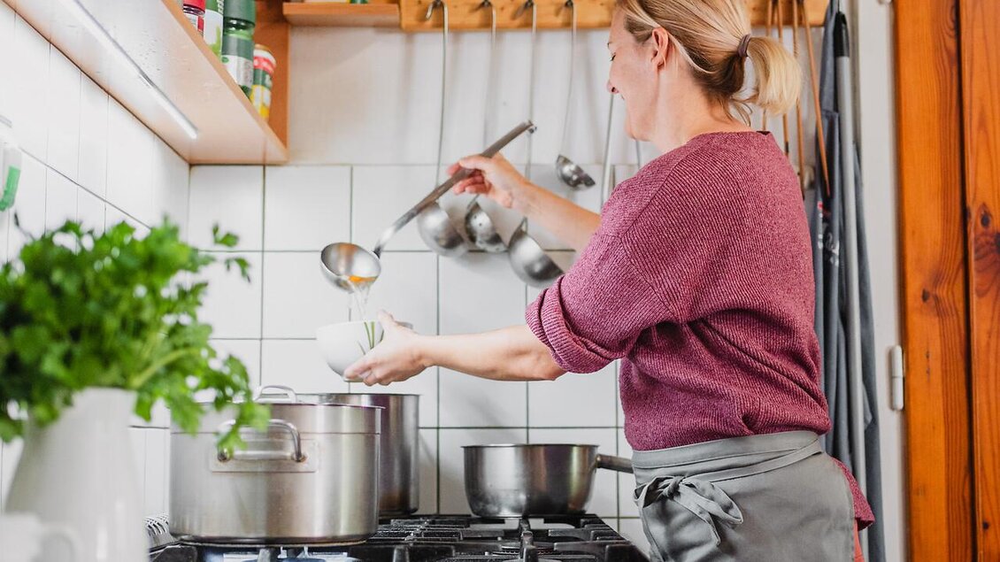 Eine Person kocht in einer modernen Küche. Töpfe stehen auf dem Herd und frische Kräuter sind auf der Arbeitsplatte sichtbar. | © TV Gesäuse