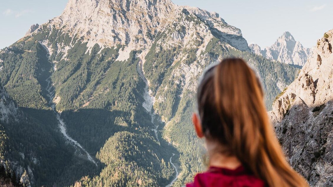 Eine Person mit einem Rucksack steht auf einem Wanderweg. Im Hintergrund sind beeindruckende Berge und ein klarer Himmel zu sehen. | © TV Gesäuse
