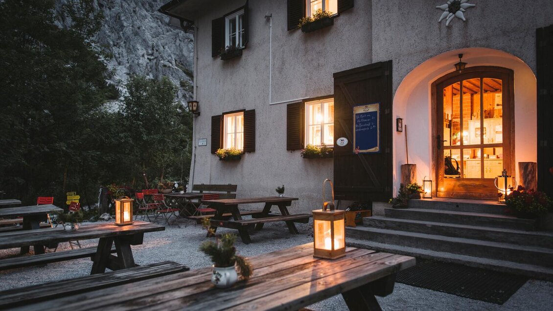 Ein gemütliches Gasthaus mit beleuchteten Fenstern und warmem Licht. Rund um die Holztische sind Laternen platziert, die eine einladende Atmosphäre schaffen. | © TV Gesäuse