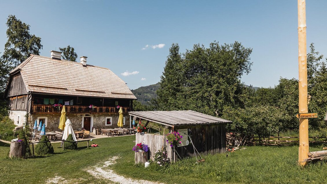 Ein charmantes Landhaus mit Holzdach und bunten Sonnenschirmen im Freien. Umgeben von grünen Wiesen und Bäumen bietet es eine einladende Atmosphäre.