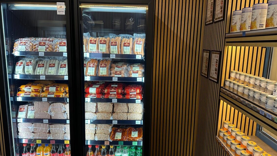 Ein Kühlschrank mit verschiedenen Lebensmitteln, darunter Snacks, Getränke und Backwaren. Neben dem Kühlschrank stehen Regale mit weiteren Produkten. | © Kaiserfleisch