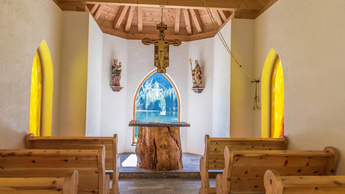 Eine kleine Kapelle mit Holzbänken und bunten Fenstern. In der Mitte befindet sich ein Altar aus Holz. | © Anita Fössl