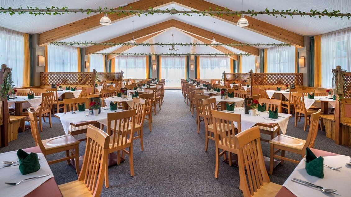 Ein einladender Restaurantbereich mit Holztischen und -stühlen. Große Fenster sorgen für viel Tageslicht und eine freundliche Atmosphäre. | © JUFA Hotels