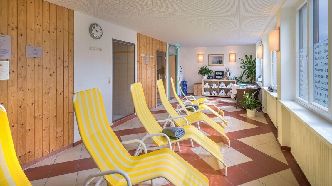 Ein heller Wellnessbereich mit gelben Liegen und Pflanzen. Die Wände sind teilweise aus Holz und der Raum wirkt einladend und entspannt. | © JUFA Hotels