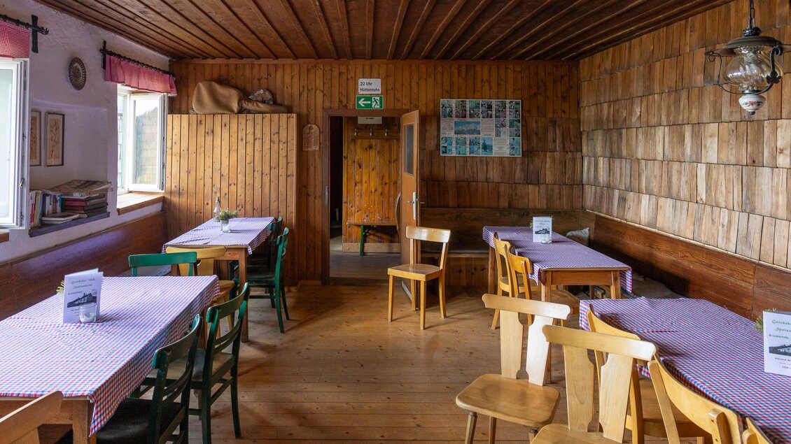 Ein gemütlicher Raum mit Holzwänden und mehreren Tischen. Die Tische sind mit karierten Tischdecken gedeckt und es gibt Stühle in verschiedenen Farben. | © TV Erzberg-Leoben