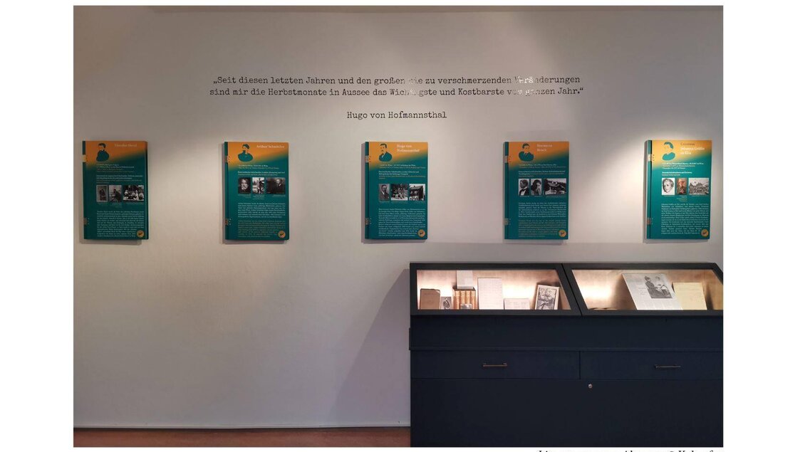 <p>Im Literaturmuseum werden die Infotaflen an der Wand und einem Vitrinenschrank ausgestellt. Die Wände sind hell gestrichen und die Tafeln sind grün mit Text und Bildern.</p> | © Kulturfux