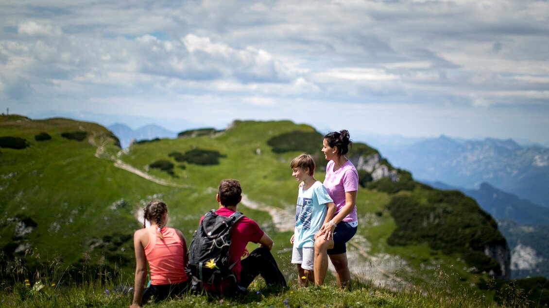Auf dem Losergipfel genießt eine Familie die Aussicht auf die umliegende Berglandschaft des Ausseerland Salzkammerguts unter blauem Himmel. | © TVB Ausseerland-Salzkammergut/Tom Lamm