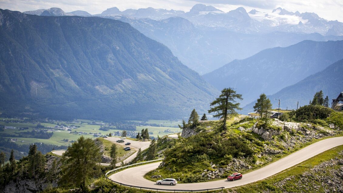 Eine kurvenreiche Straße durch die Berge mit grünen Wiesen und hohen Gipfeln im Hintergrund. Die Landschaft ist malerisch und zeigt die Schönheit der Natur. | © TVB Ausseerland - Salzkammergut-Tom Lamm