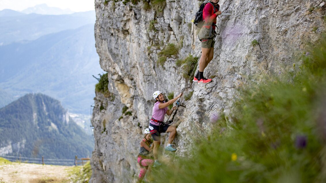 Drei Kletterer besteigen eine steile Felswand in den Bergen. Im Hintergrund sind malerische Landschaften mit Hügeln und Tälern zu sehen. | © Loser Bergbahnen Altaussee/T. Lamm
