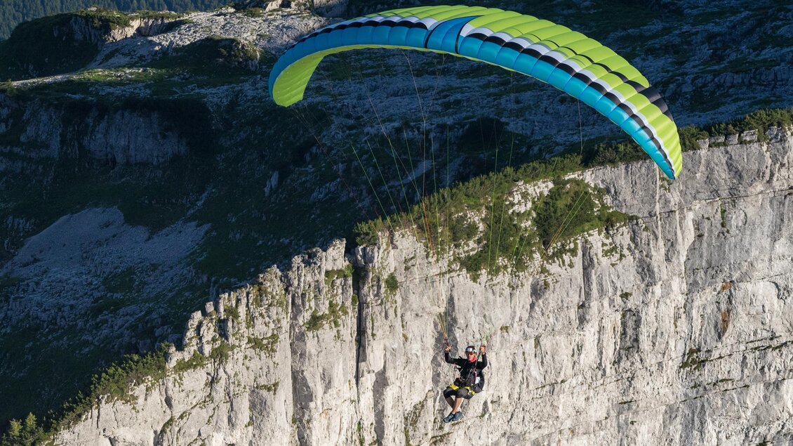 Ein Gleitschirmflieger schwebt über einer steilen Felswand. Der Sonnenlicht gibt der Szenerie ein dramatisches Licht. | © Loser Bergbahnen Altaussee/F. Loitzl