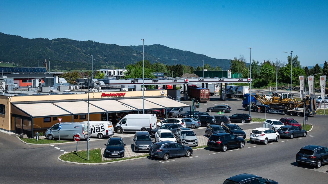 Ein Parkplatz vor einem Restaurant mit mehreren Autos. Im Hintergrund sind Berge und eine klare blaue Himmel sichtbar. | © M-Rast