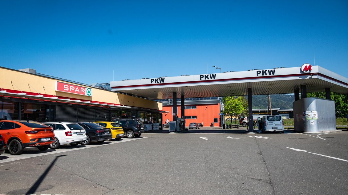 Eine Tankstelle mit mehreren Fahrzeugen davor und einem Supermarkt in der Nähe. Der Himmel ist klar und blau. | © M-Rast