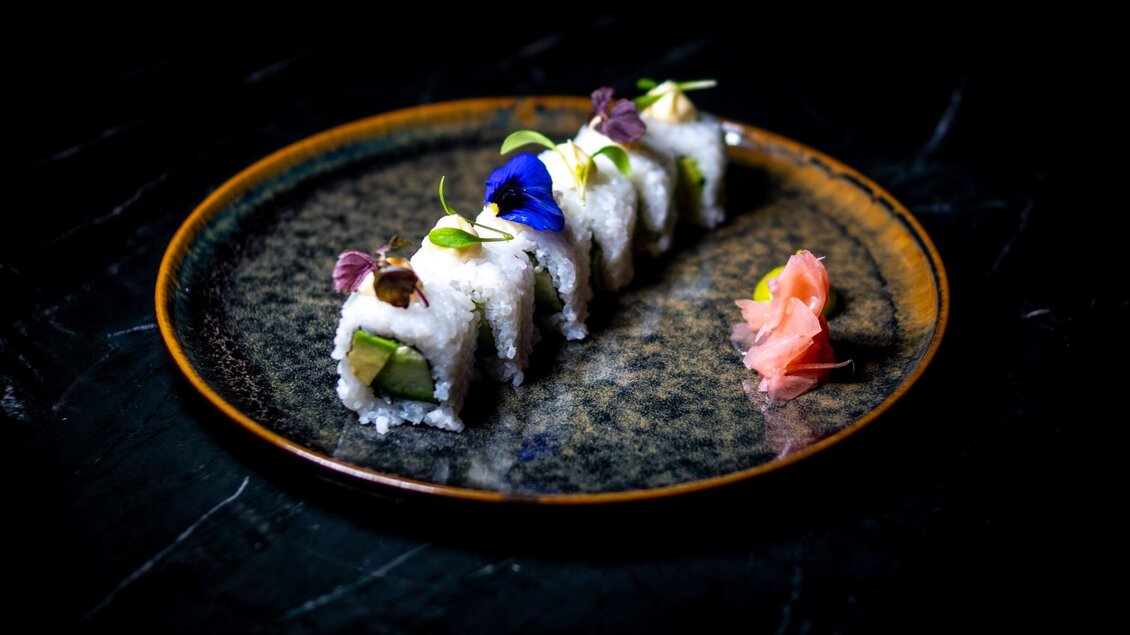 Modern angerichtete Sushi-Rollen im Restaurant Miss Cho  mit essbaren Blüten und Ingwer auf dunklem Teller in der Bar Amouro in Graz. | © Miss Cho - aiola