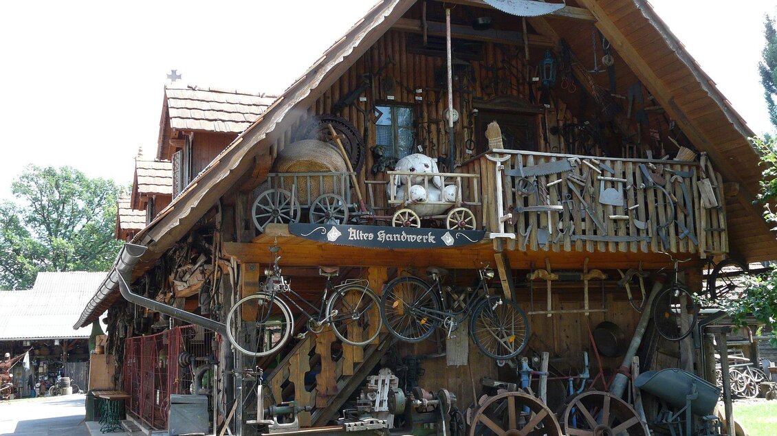 Ein traditionelles altes Holzhaus, das mit verschiedenen Werkzeugen und Fahrrädern dekoriert ist. Die Umgebung wirkt ländlich und einladend. | © Familie Wiedner