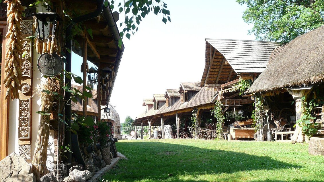Eine malerische Szene mit traditionellen, strohgedeckten Häusern in einer grünen Umgebung. Das Licht scheint hell und es gibt viele Pflanzen rundherum. | © Familie Wiedner