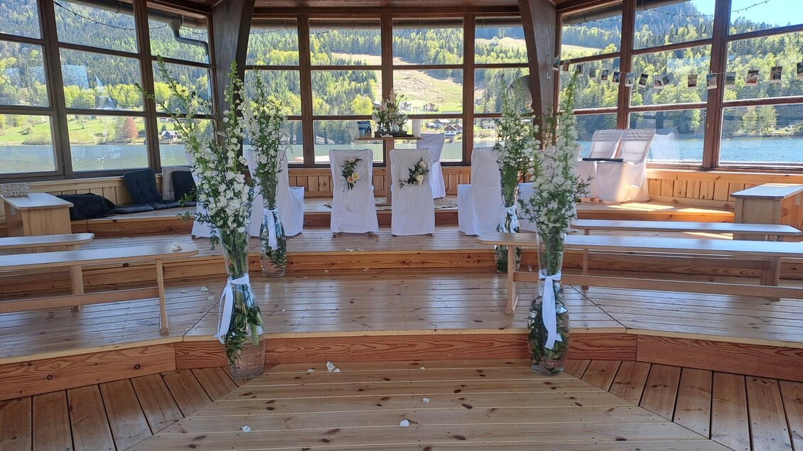 Ein festlich dekorierter Bereich mit weißen Stühlen und Blumenarrangements. Der Blick auf den See und die umliegenden Berge schafft eine romantische Atmosphäre. | © Theresa Grill
