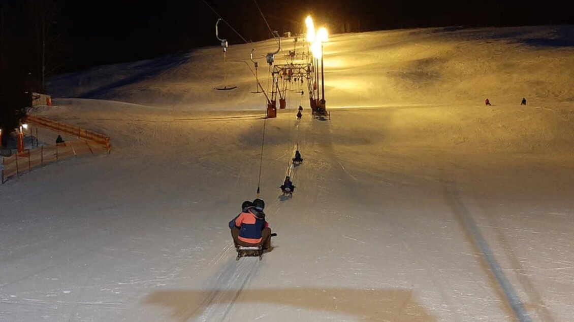 Eine beleuchtete Skipiste nachts mit Menschen auf einem Lift. Der Schnee glitzert im Schein der Lichter. | © Schilift Zlaim