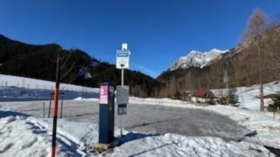 Eine ruhige Winterlandschaft mit Schnee und Bergen im Hintergrund. An einer Haltestelle stehen Informationen und Zahlungsmöglichkeiten. | © Hanna Giraudo