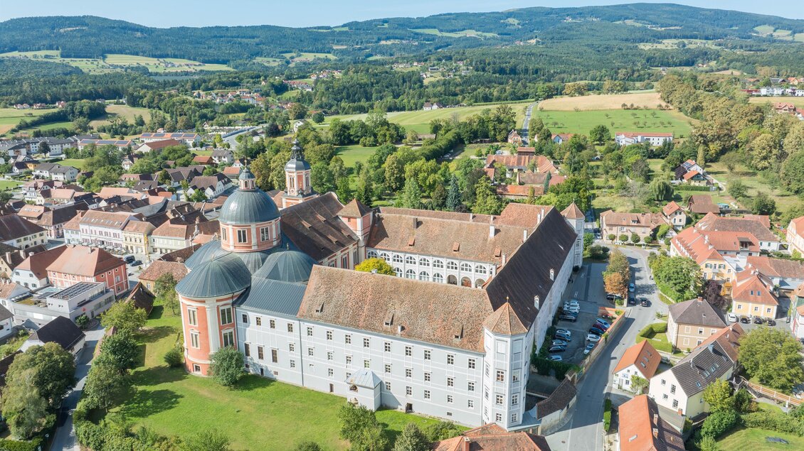 Eine beeindruckende Klosteranlage mit Kuppeln und großen Gebäuden. Umgeben von grünen Wiesen und einer ländlichen Landschaft.