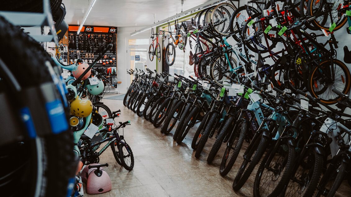 Ein Fahrradgeschäft mit einer Vielzahl von Fahrrädern und Accessoires. An den Wänden hängen Fahrräder, während weitere im Gang aufgestellt sind. | © Radwerkstatt Willibald