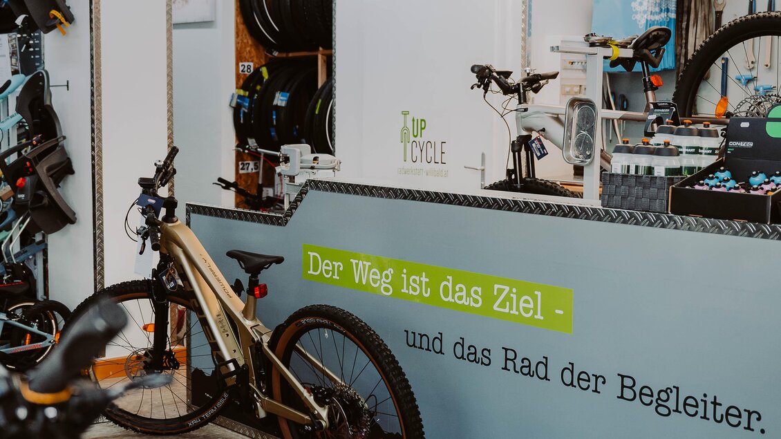 Ein Fahrradgeschäft mit verschiedenen Fahrrädern und Zubehör. An der Wand steht der Spruch: "Der Weg ist das Ziel - und das Rad der Begleiter." | © Radwerkstatt Willibald