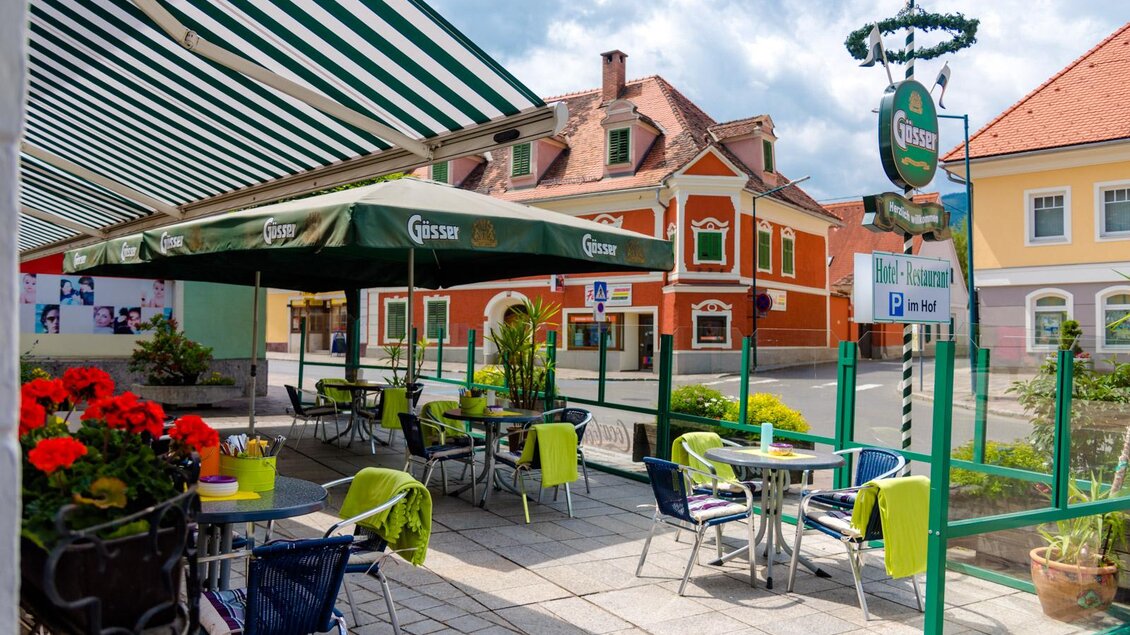 Ein gemütlicher Außenbereich mit Tischen und Stühlen in einem Restaurant. Im Hintergrund sind farbenfrohe Gebäude und eine einladende Atmosphäre zu sehen. | © Landhotel  Groggerhof
