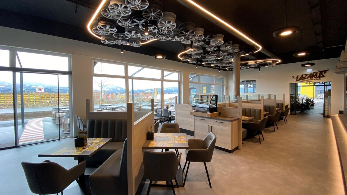 Ein modernes Restaurant mit stilvollen Sitzbereichen und großen Fenstern. Die Decke ist mit dekorativen Elementen ausgestattet, die dem Raum eine einzigartige Atmosphäre verleihen. | © Ring Rast Betriebs-GmbH