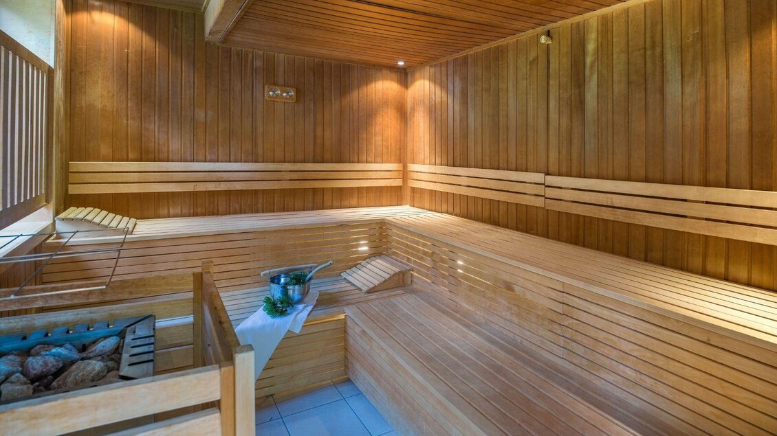 Eine gemütliche Sauna mit Holzverkleidung und Bänken. Auf einem Tisch steht ein Kübel mit Wasser und Saunasteinen. | © JUFA Hotels